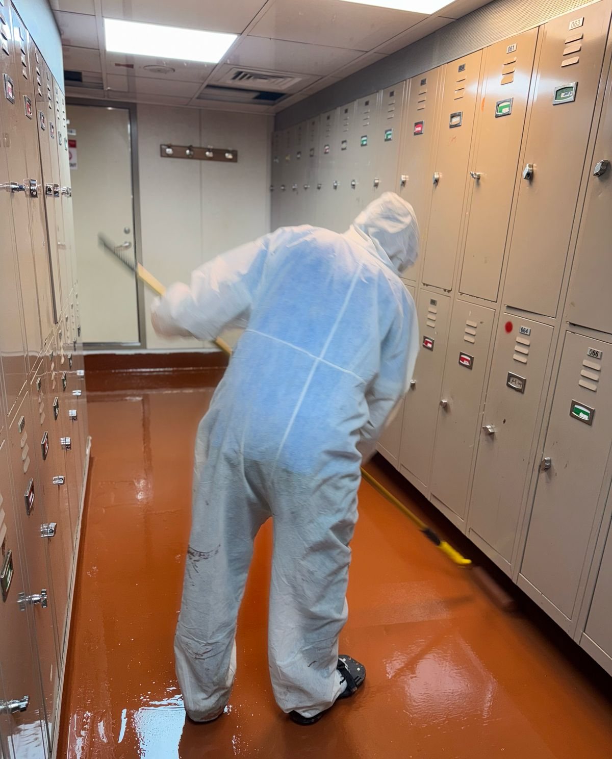 Crew applying epoxy floor coating in a locker room